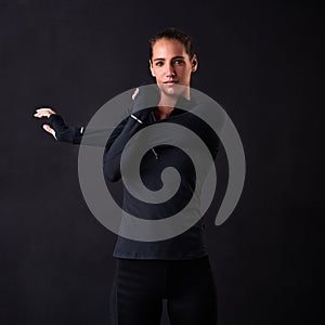 Get focused, get fit. Studio portrait of a young woman in gym clothes stretching her arms against a dark background.