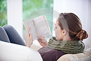 Get lost in a good book. Rear-view shpt of a woman reading a book at home.