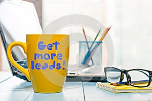 Get more leads motivation phrase on yellow cup of morning coffee or tea at business office workplace backgound. With