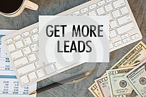 GET MORE LEADS is written in a document on the office desk, coffee, money and smartfon