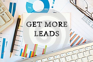 GET MORE LEADS is written in a document on the office desk, diagram and keyboard