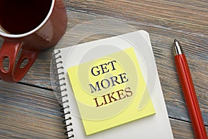 Get More Likes concept. Notebook page with text, red pencil and coffee cup. Office desk table top view