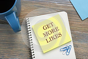 Get More Likes concept. Notebook page with text, red pencil and coffee cup. Office desk table top view