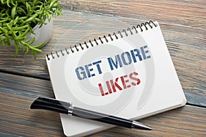 Get More Likes concept. Notebook page with text, red pencil and coffee cup. Office desk table top view