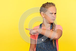 Get out! Portrait of angry upset little girl with braid in denim overalls pointing way out showing exit