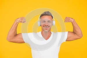 Get powerful sounds. Strong man flex arms yellow background. Headphones technology. Modern workout and training. Force