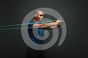 Get stronger every day. Sportsman working out with resistance band over dark background