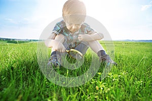 Get to know the world. Everything is incredible near you. Young boy exploring nature in a meadow with a magnifying glass