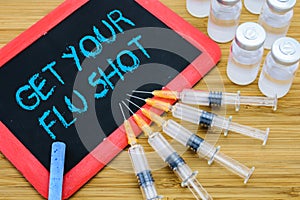 Get Your Flu shot written on chalkboard with vaccine in syringes