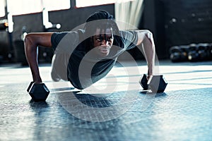 He gets stronger with each day. a young man doing push ups with dumbbells in a gym.