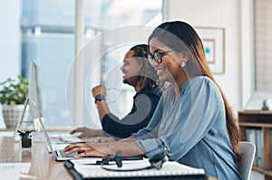 Getting ahead in the game. a young businesswoman working on a laptop in an office with her colleague in the background.