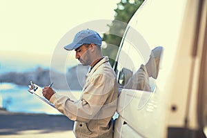 Getting all his logistics down. a delivery man writing on a clipboard while standing next to his van.