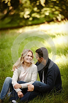Getting away for a loving moment together. a loving young couple sitting on the grass in a park.
