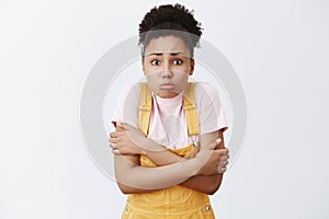 It is getting chilly, lend me coat. Portrait of cute timid dark-skinned girlfriend in summer yellow overalls, hugging