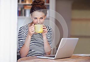 Getting a creativity boost from caffiene. a young woman working on her laptop and enjoying a cup of coffee at home.