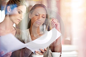 Getting down to business with coffee. Two women discussing paperwork during a business meeting at a cafe.