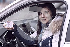 Getting a driver`s license, female hands show US driving license, amid the steering wheel of a car