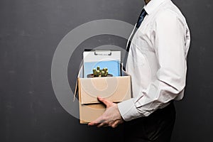 Getting fired. Cropped image of handsome businessman in formal wear holding a box with his stuff, on gray background