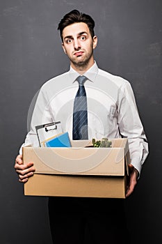 Getting fired. Handsome businessman in formal wear holding a box with his stuff, on gray background