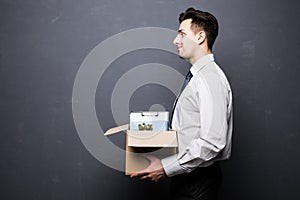 Getting fired. Side view of handsome businessman in formal wear holding a box with his stuff, on gray background