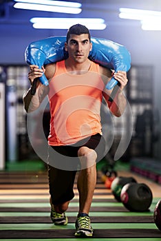 Getting a full body workout with a sandbag. a young man working out with a sandbag at the gym.