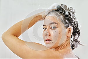 Getting her hair squeaky clean. Shot of a young woman washing her hair with shampoo in the shower at home.
