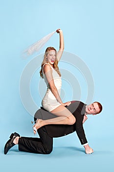 Getting married. Happy, excited young woman sitting on man& x27;s back against blue studio background. Happy wife