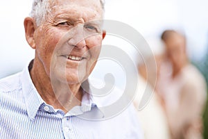 Getting older...but also happier. Portrait of a senior man standing outside with people blurred in the background.