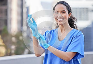 Getting ready for a checkup. Shot of a young female doctor putting on gloves against a city background.