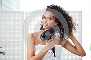 Getting ready for a good hair day. an attractive young woman blowdrying her hair at home.