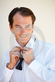 Getting ready for his big day. A handsome young man tying his bow tie.