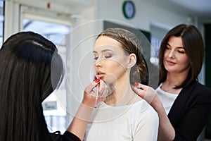 Getting ready for party. Young pretty girl sitting in beauty salon while hairdresser and make-up artist making her look beautiful