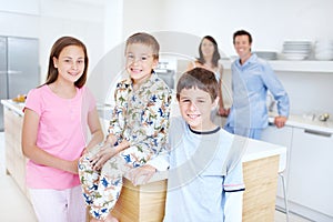 Getting ready to eat a wholesome breakfast. Three children in the kitchen with their parents standing blurred in the