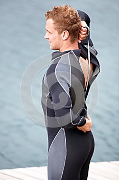 Getting ready to get wet. Young man putting on his wetsuit before engaging in some watersports.