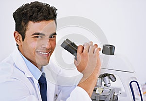 Getting results in the lab. Portrait of a smiling lab technician using a microscope while sitting in a lab.