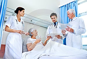 Getting a second opinion. three doctors attending a senior patient who is in a hospital bed.