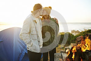 Getting their camp warmed up. an affectionate young couple getting warm by the fire.