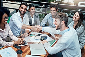 Getting together to better business. businesspeople shaking hands during a meeting at a cafe.