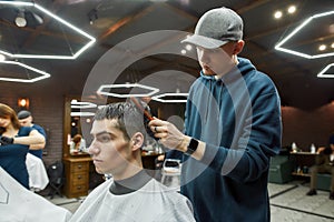 Getting trendy haircut. Side view of a professional barber drying the hair of a handsome guy in the modern barbershop