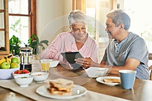 They are getting used to this new contraption. a cheerful elderly couple browsing on a digital tablet together while