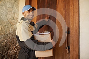 Getting your package delivered on time every time. Portrait of a smiling delivery man holding a package and knocking on