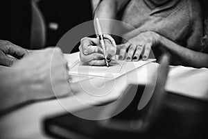 Ggreyscale image of a female signing a legal document with a pen in her hand