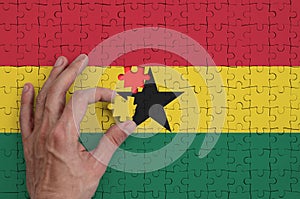 Ghana flag is depicted on a puzzle, which the man`s hand completes to fold