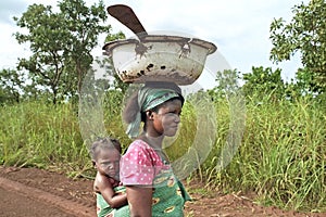 Ghanaian Woman lugging child and kitchen utensils