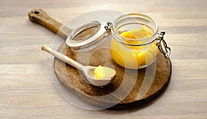 Ghee clarified butter desi in glass jar with spoon made from wood on natural wooden background