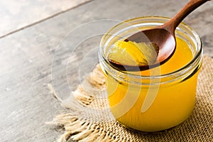 Ghee or clarified butter in jar and wooden spoon on woode. Copyspace photo