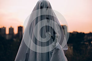 Ghost holding wilted flower standing against evening city