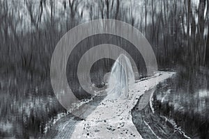 A ghostly, hooded, white robed figure standing on a snowy forest path in winter. With a blurred, artistic textured black and white photo