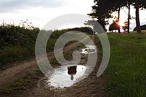 The ghostly silhouette of a person who isn`t there, reflected in a puddle on a country path at sunset