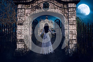 Ghostly woman in torn white dress facing away in the gateway of a creepy old Victorian mansion house. 3D illustration